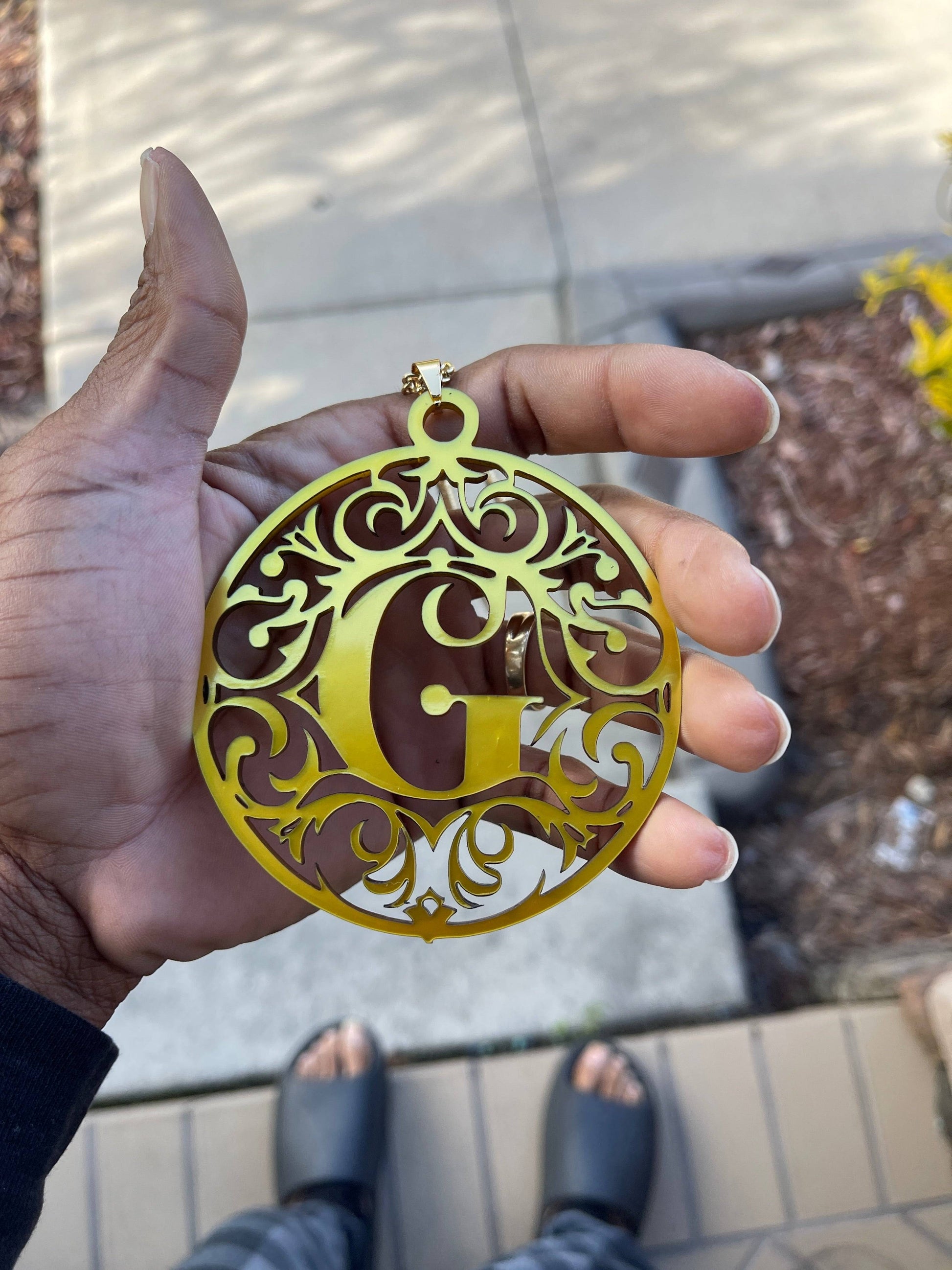 a person holding a gold acrylic letter g medallion