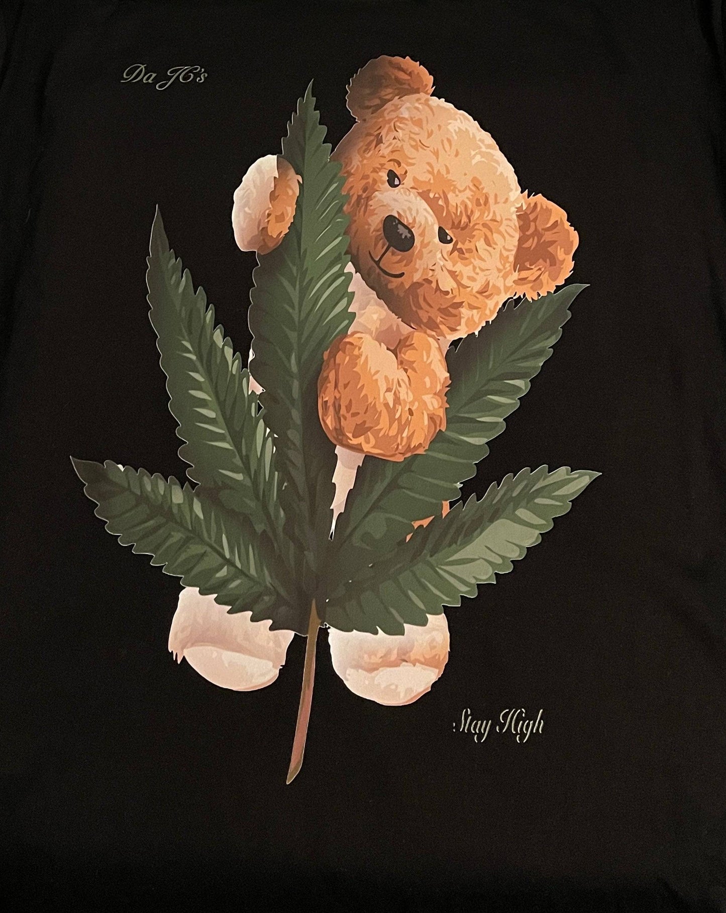 a t-shirt with a brown teddy bear sitting on top of a green leaf